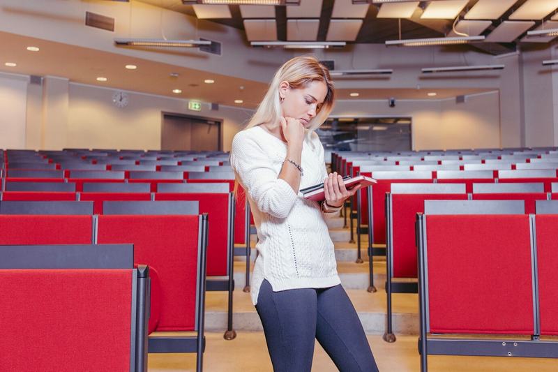 Женщина стоит в пустом лекционном зале и читает книгу.